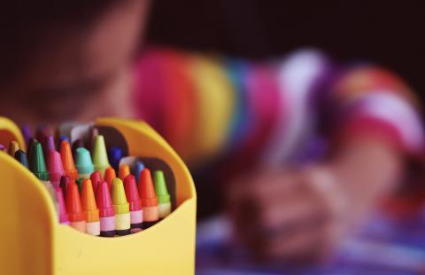 A colorful box of crayons in front of student drawing