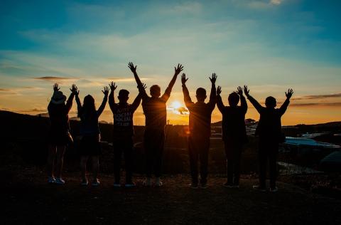 Group of youth reaching arms up into the sunset