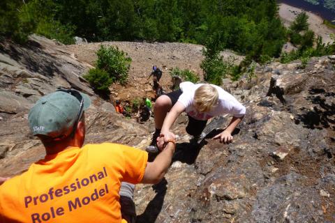 Youth scrambling up on a steep rock.