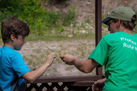 A boy and a camp counselor preparing for target practice by putting on hearing protection.