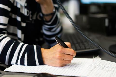 Person writes while talking on phone