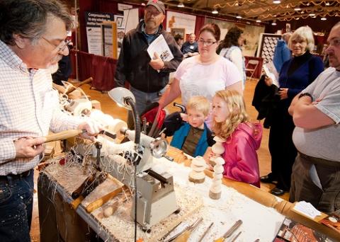 adults and youth watching a craftsman using a wood turning lathe