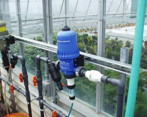 A blue fertilizer injector at the wall of a commercial greenhouse.