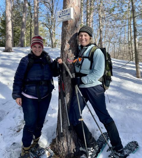 Gail Wigler and Katie Stuart standing by a tree in the winter