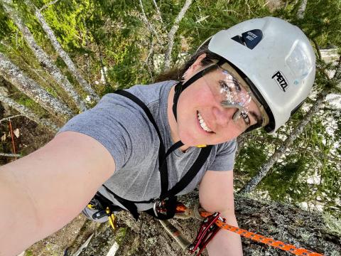 Lindsay Watkins in a tree canopy wearing a helmet and safety glasses