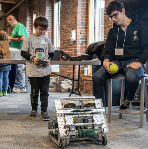 Child controlling robot with remote while volunteer observes