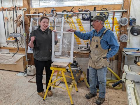 Instructor and intern standing with a wooden window sash in a woodworking shop