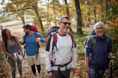 Four people wearing backpacks walking on a trail in the fall