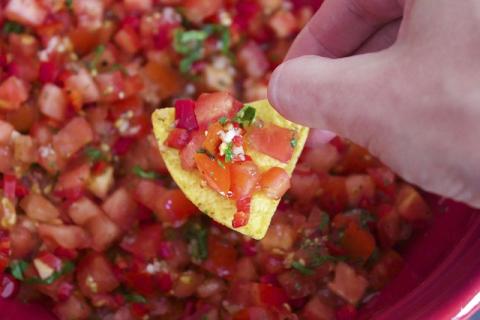 A big bowl of salsa with a chip in a persons hand
