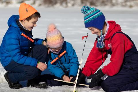 Three children ice fishing in winter