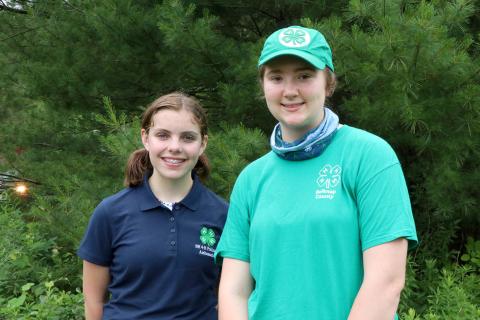 Two teen girls wearing 4-H shirts, standing in front of trees