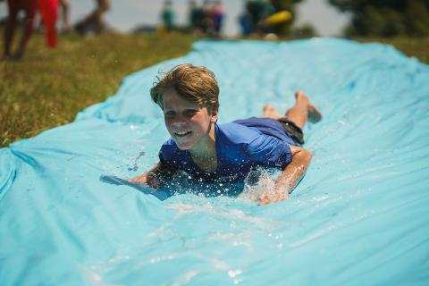 Boy sliding head first down tarp filled with water