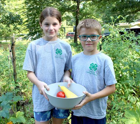 A girl and boy holding bowl of produce in their garden