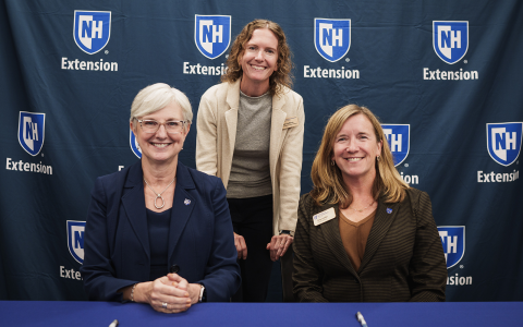 Three people in front of a blue banner with UNH Extension logos for an official signing ceremony.