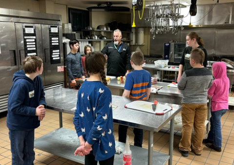 group of kids in an industry kitchen taking instruction from Chef