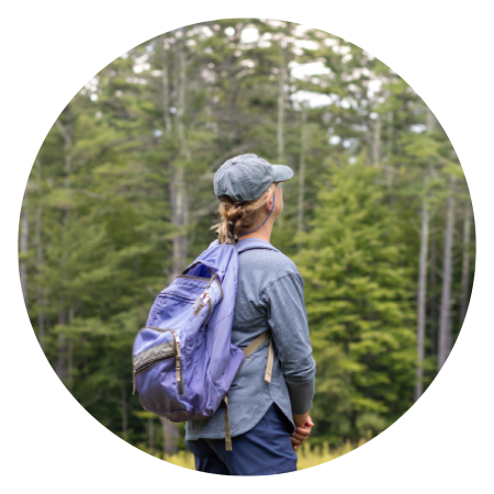 woman standing in the woods wearing a hat and backpack