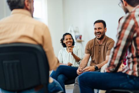 An adult man, looking happy, talking with random people from the group therapy.