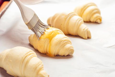 brushing egg wash on uncooked croissants