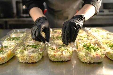 person with gloved hands packaging salads into plastic containers