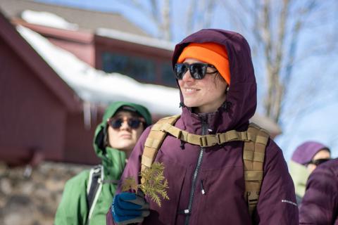 a woman wearing an orange hat smiles while holding tree needles