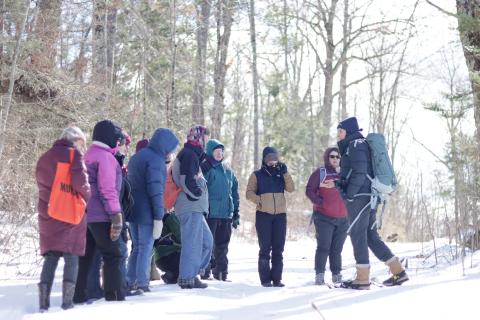 a group of women, some wearing snowshoes, looking for wildlife tracks in the snow