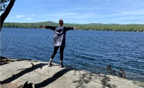 Person with stretched arms standing on a rock, during a mindful moment overlooking the lake at Belmont Beach.