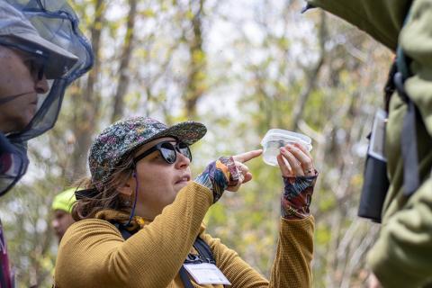 Extension staff member Charlotte Thompson points at a specimen in a plastic container in the forest