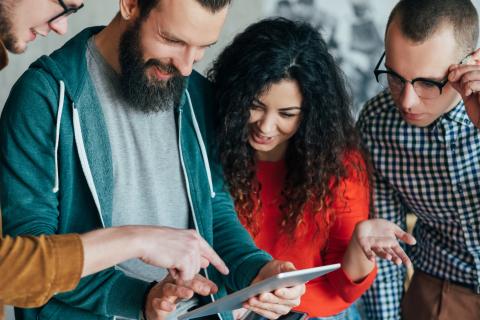 Group of happy millennials looking at tablet. Think big to reach goals.