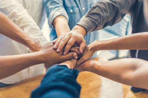 seven people standing in a circle shown from the elbow down with their hands piled in the center