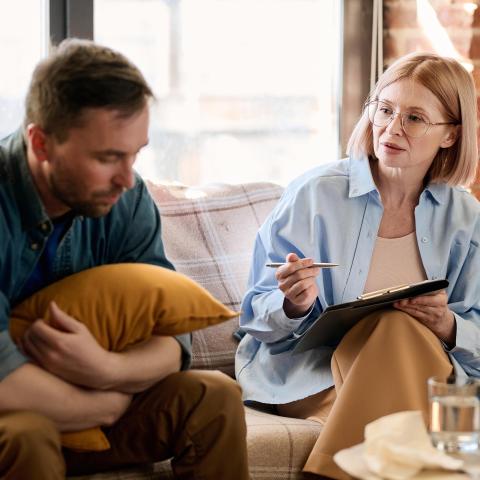 Adult Male holding a pillow talking to a female counselor