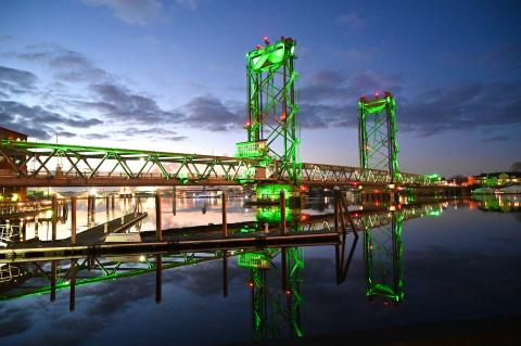 Bridge over a river illuminated in green with reflection on the water.