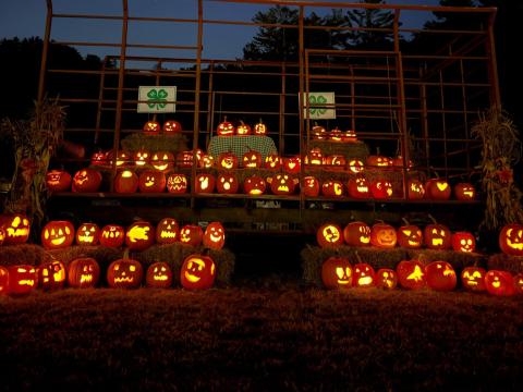 lit pumpkins line a hay wagon with two 4-H clover signs in the back
