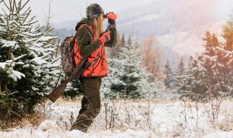 woman in hunting gear using binoculars in wintertime