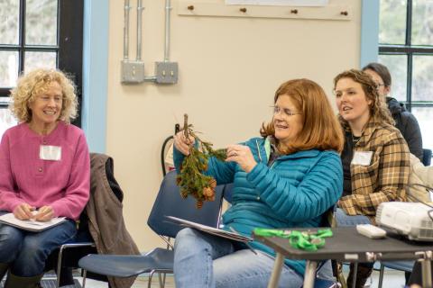 women sitting in a classroom passing around a hemlock branch