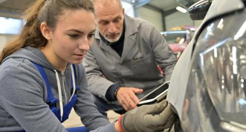 An instructor helps a student work on a car