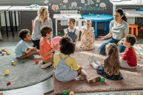 Children in circle time with teachers, engaging in a classroom activity.