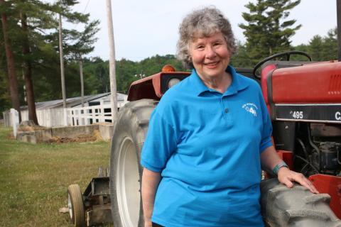 Former Rockingham County 4-H Extension Educator Lynn Garland poses next to a tractor. She is wearing a blue shirt and smiling at the camera.