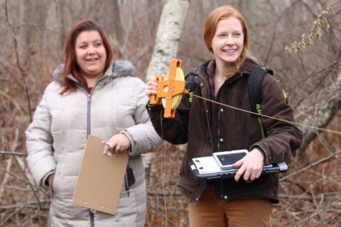 Volunteer and graduate student in woods with clipboard and measuring tape