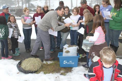 Students interact with adult observing hay in the winter snow
