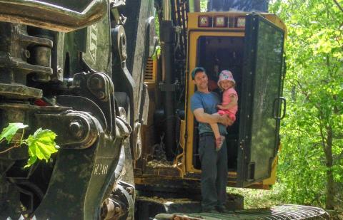 Greg with his daughter in front of forestry equipment