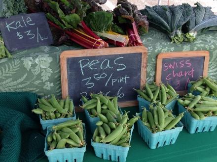 Cartons of peas and bundles of kale for sale at a farmers market.