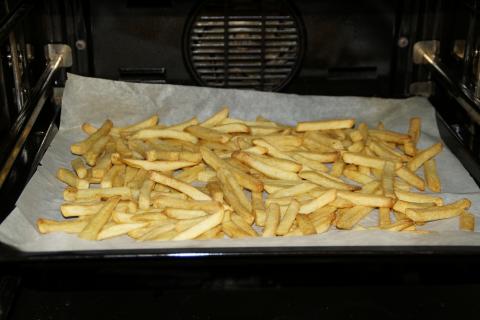 French fries on cookie sheet lined with parchment paper on oven rack.