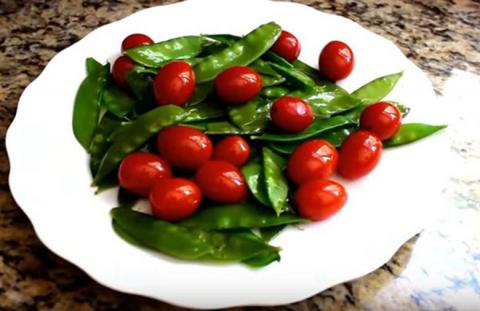 Snow peas and tomatoes on a white plate.