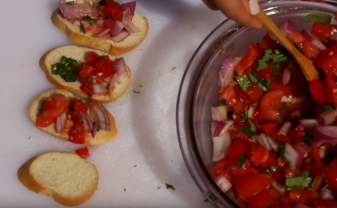 Bowl of freshly made tomato bruschetta, being spooned onto small rounds of bread.