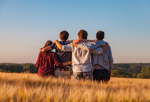 Four friends standing in field with arms over one another's shoulders 