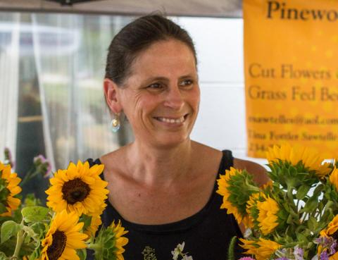 A woman farmer is standing and smiling behind her display of sunflowers