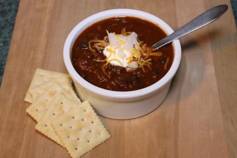 Bowl of chili with dollop of greek yogurt and shredded cheese on top, with saltine crackers on the side.