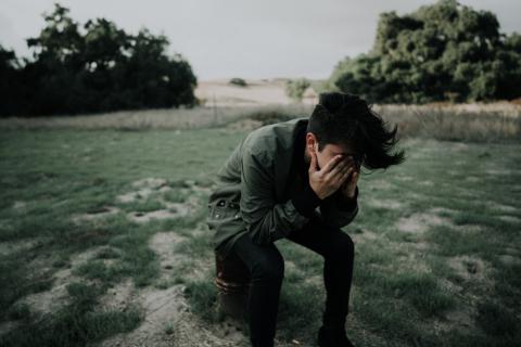 boy sitting in field hiding face