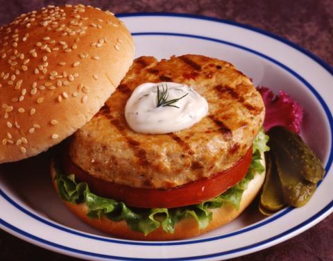 Alaskan salmon burger recipe prepared on a bun with lettuce and tomato.