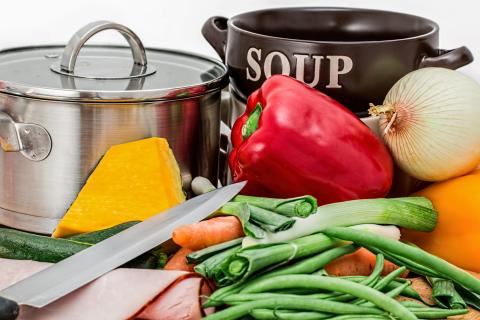 Stock pot with knife, fresh vegetables, meat and soup bowl.